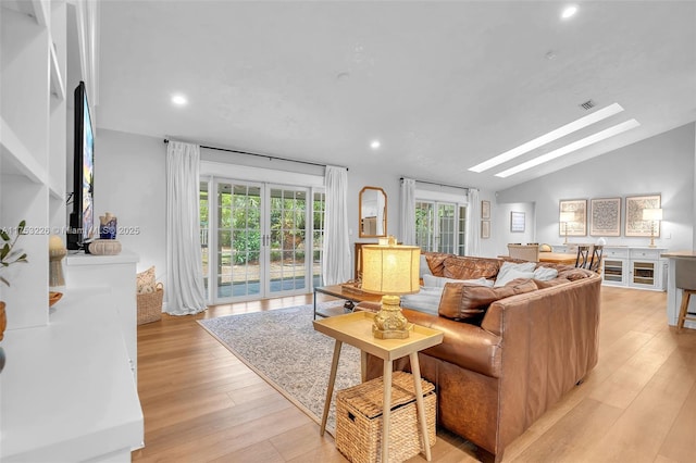 living room with visible vents, vaulted ceiling with skylight, recessed lighting, and light wood-type flooring