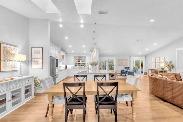 dining room with light wood-type flooring, visible vents, and lofted ceiling with skylight