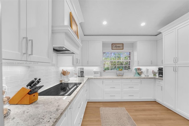 kitchen featuring light wood finished floors, black electric stovetop, custom range hood, white cabinets, and decorative backsplash