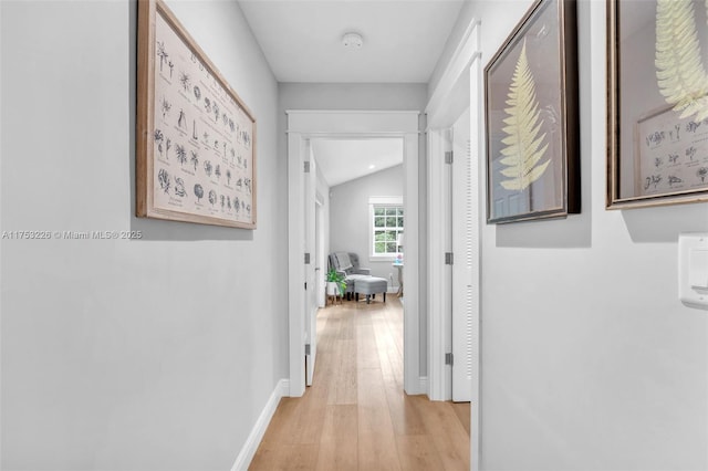 hallway with baseboards, vaulted ceiling, and light wood-style floors
