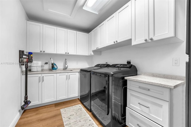 clothes washing area featuring cabinet space, attic access, a sink, light wood-type flooring, and washing machine and dryer