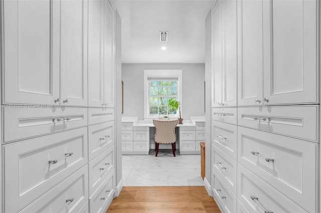 spacious closet with built in study area, visible vents, and marble finish floor