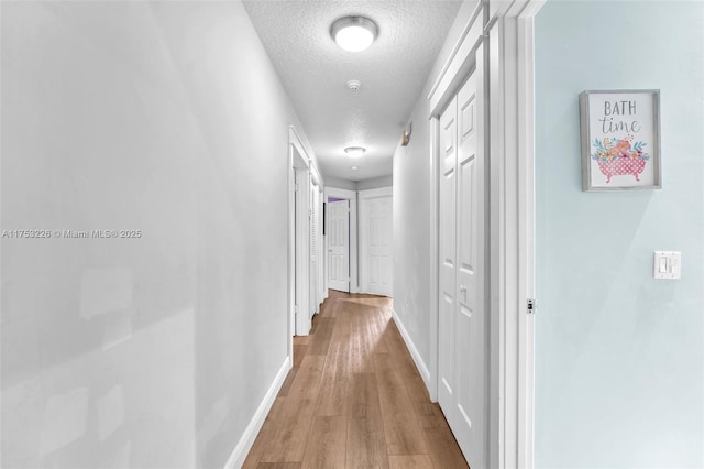 hall featuring baseboards, wood finished floors, and a textured ceiling