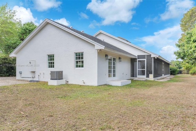 back of property with stucco siding, a sunroom, a lawn, and french doors