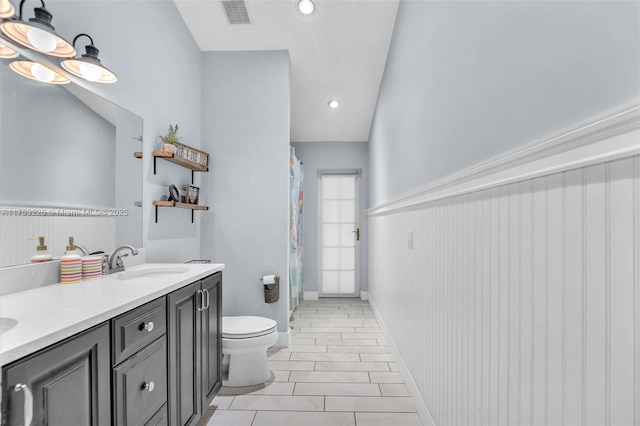 bathroom with toilet, a sink, wainscoting, visible vents, and double vanity