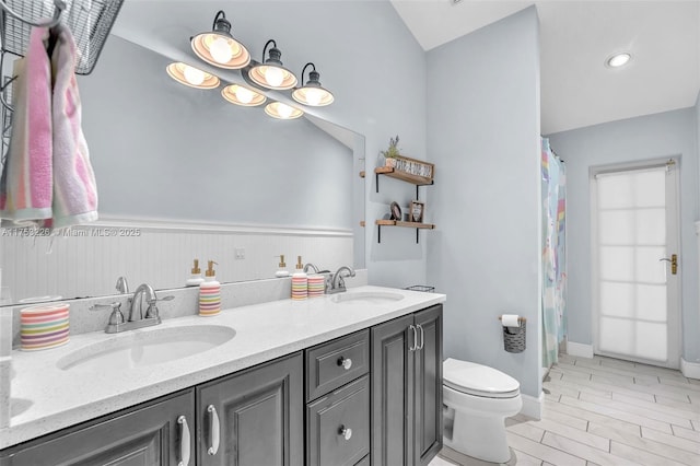 bathroom with toilet, a sink, double vanity, and wainscoting