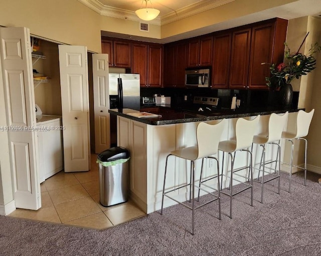 kitchen with ornamental molding, washer / dryer, a peninsula, a kitchen bar, and appliances with stainless steel finishes
