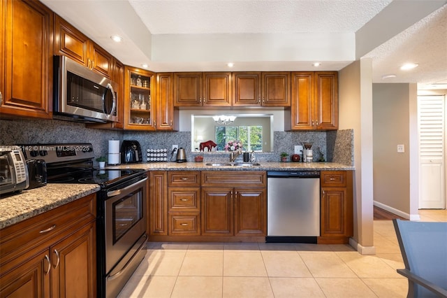 kitchen with light tile patterned floors, brown cabinets, appliances with stainless steel finishes, and light stone counters
