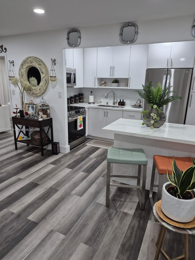 kitchen with a breakfast bar, a sink, light countertops, appliances with stainless steel finishes, and backsplash