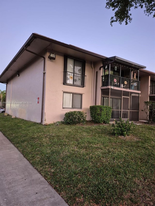 exterior space with a balcony, a yard, a sunroom, and stucco siding