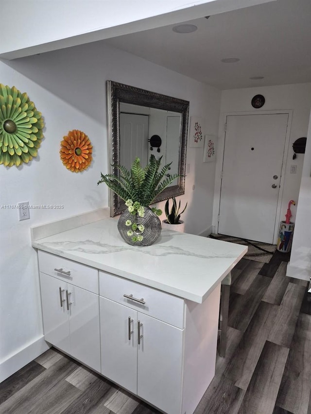 kitchen featuring dark wood-type flooring, white cabinets, light stone counters, and baseboards