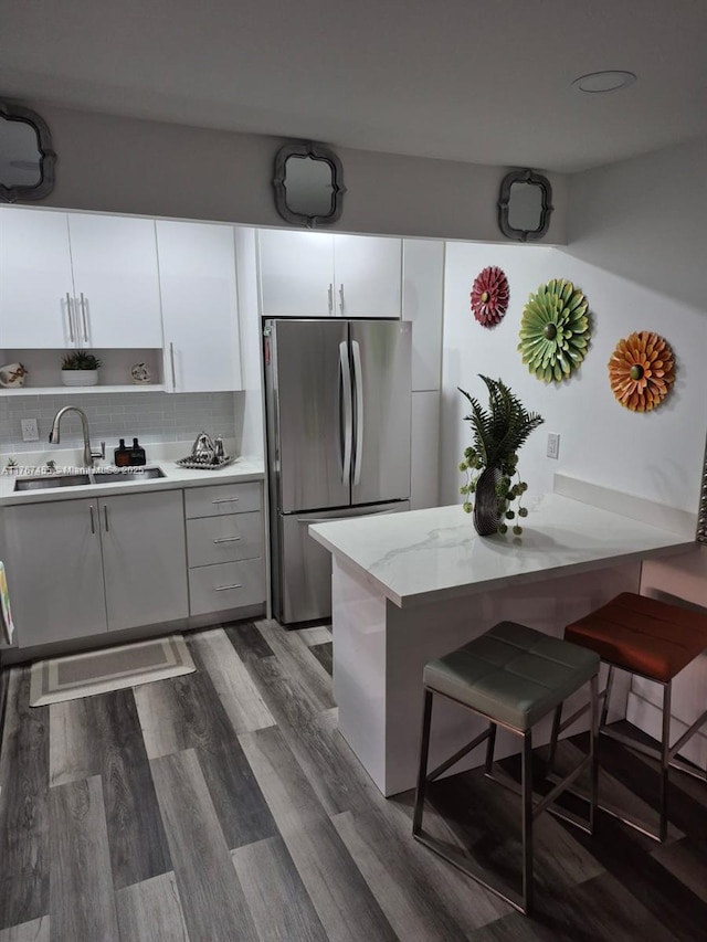 kitchen featuring a sink, tasteful backsplash, dark wood-style floors, freestanding refrigerator, and white cabinets