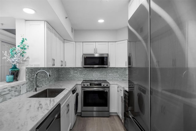 kitchen featuring light stone counters, washer / clothes dryer, a sink, stainless steel appliances, and tasteful backsplash