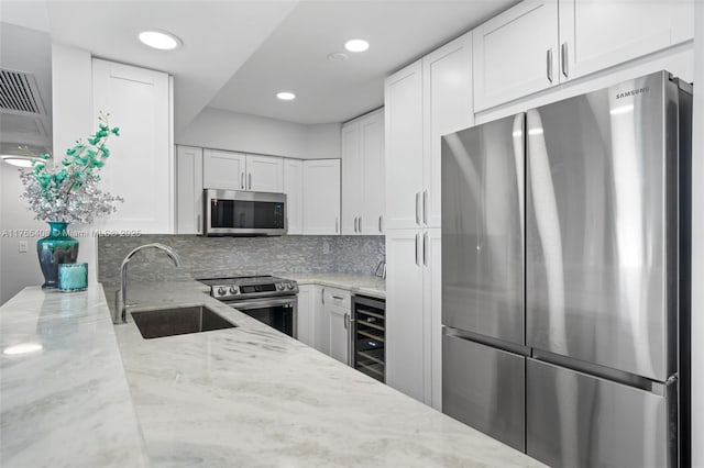 kitchen with a sink, wine cooler, appliances with stainless steel finishes, white cabinets, and light stone countertops