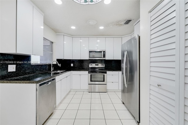 kitchen with visible vents, modern cabinets, a sink, dark countertops, and appliances with stainless steel finishes