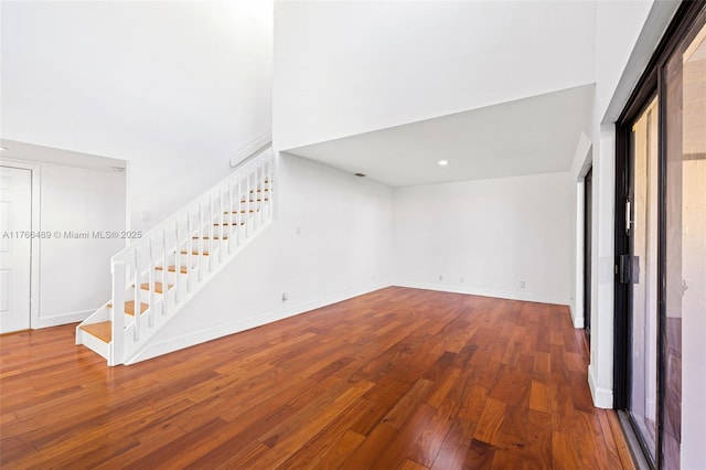 spare room featuring a high ceiling, stairway, baseboards, and wood-type flooring