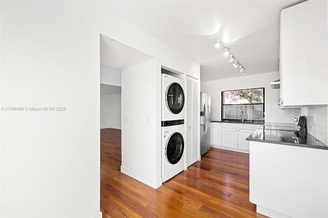 laundry area with laundry area, stacked washer / dryer, dark wood-style floors, and a sink