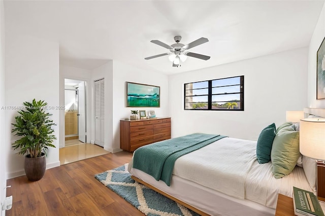 bedroom with a ceiling fan, wood finished floors, baseboards, a closet, and ensuite bathroom