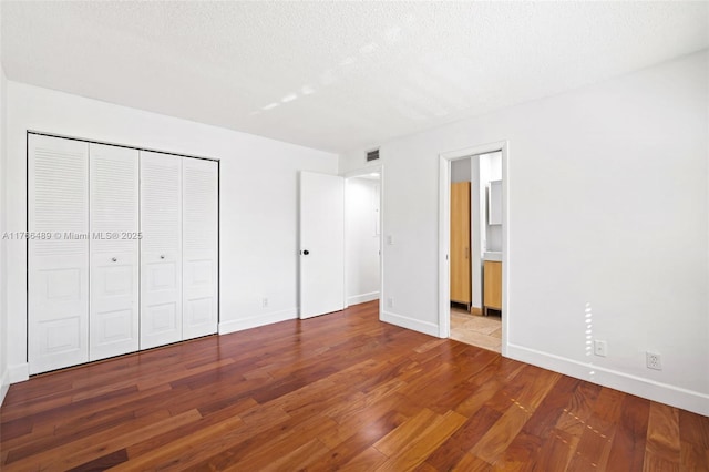 unfurnished bedroom with a closet, baseboards, a textured ceiling, and wood finished floors
