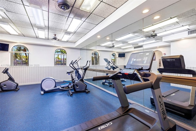 gym with a wainscoted wall, visible vents, and a drop ceiling