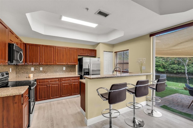 983 SW 143rd Ave Unit 1403, Pembroke Pines, FL 33027 - kitchen with stainless steel appliances, light wood-type flooring, a raised ceiling, a breakfast bar area, and decorative backsplash