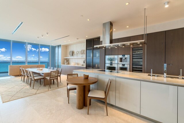 kitchen with double oven, light countertops, island range hood, modern cabinets, and expansive windows