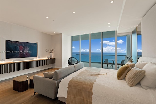 bedroom with recessed lighting, wood finished floors, a water view, expansive windows, and multiple windows