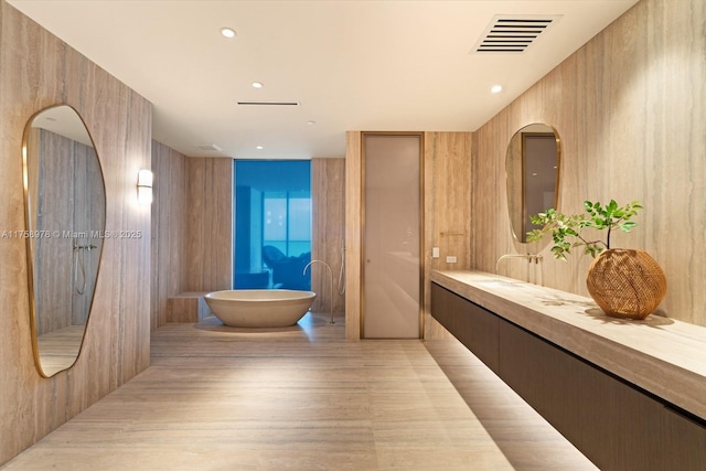 bathroom with a freestanding tub, wood finished floors, visible vents, and vanity