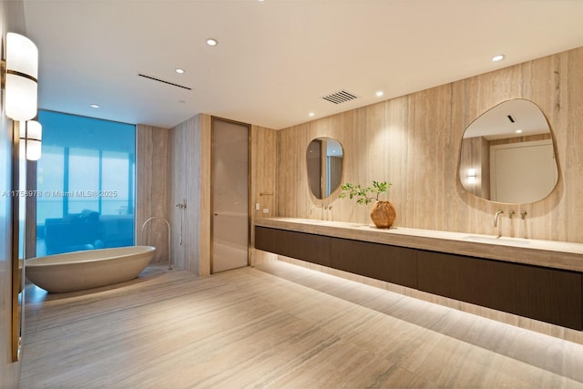 full bath featuring a sink, double vanity, a freestanding bath, visible vents, and wood finished floors