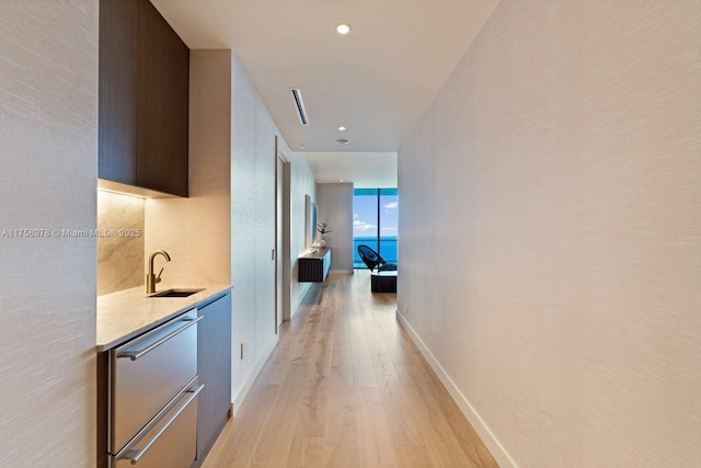 hallway with recessed lighting, light wood-style floors, baseboards, and a sink