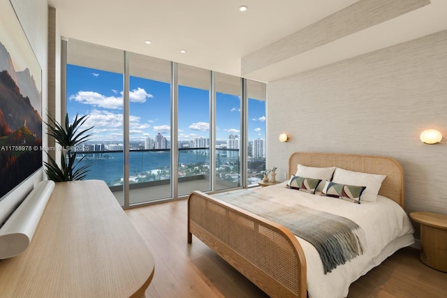 bedroom featuring a city view, a wall of windows, wood finished floors, and access to exterior