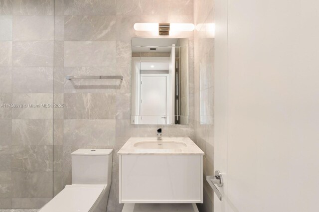 bathroom with tile walls, vanity, and toilet