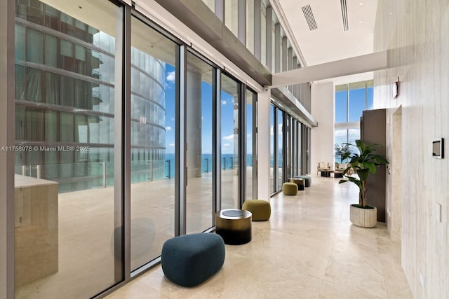 interior space featuring a wall of windows, a water view, a high ceiling, and visible vents