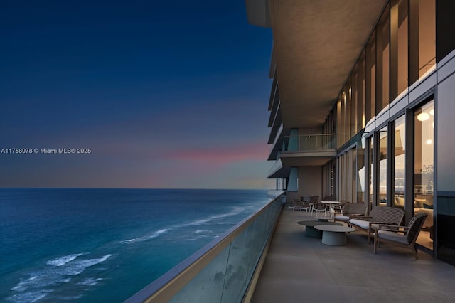 balcony at dusk featuring a water view