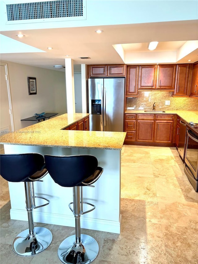 10410 S Ocean Dr Unit 504, Jensen Beach, FL 34957 - kitchen featuring appliances with stainless steel finishes, a breakfast bar, light stone counters, brown cabinetry, and decorative backsplash