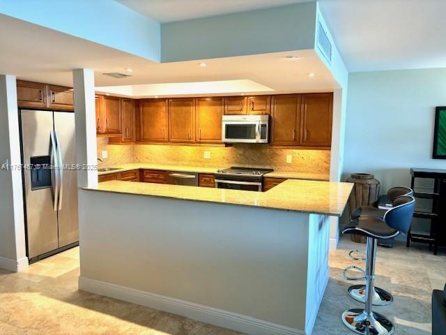 10410 S Ocean Dr Unit 504, Jensen Beach, FL 34957 - kitchen with appliances with stainless steel finishes, decorative backsplash, brown cabinetry, a kitchen bar, and a spacious island
