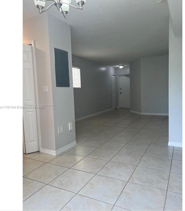 empty room featuring electric panel, a notable chandelier, baseboards, and light tile patterned floors