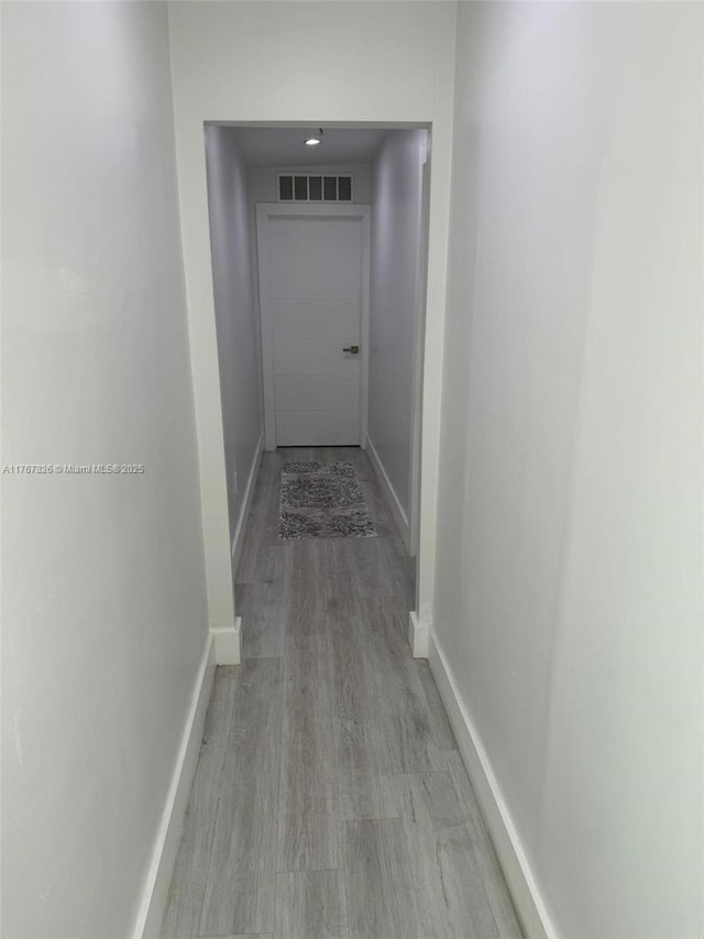 hall with light wood-style flooring, baseboards, and visible vents