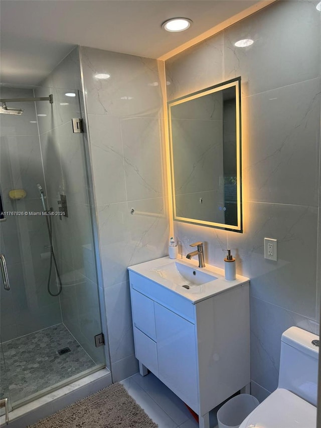 bathroom with vanity, tile walls, toilet, a shower stall, and tile patterned floors