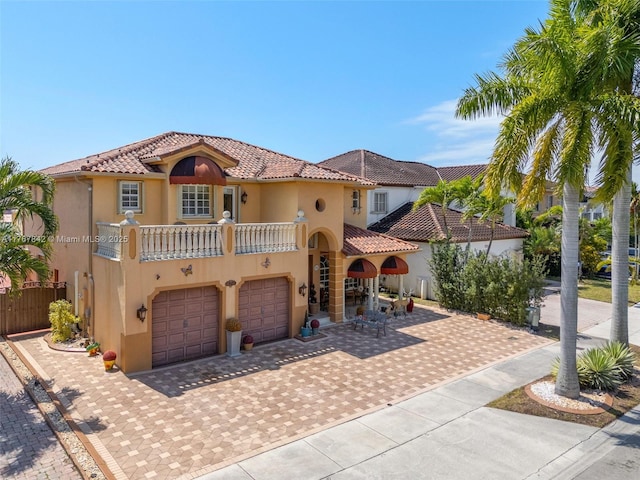 mediterranean / spanish home with a balcony, an attached garage, stucco siding, a tile roof, and decorative driveway