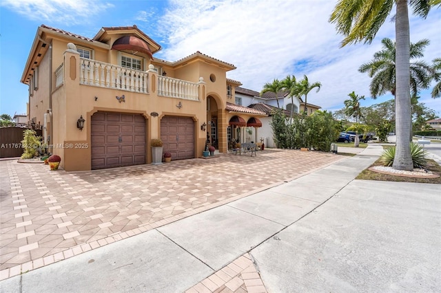 mediterranean / spanish-style house with a tile roof, stucco siding, decorative driveway, a balcony, and an attached garage