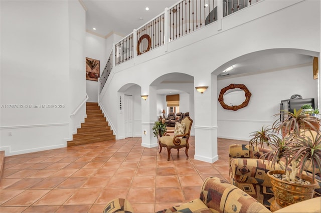 interior space with ornamental molding, stairway, light tile patterned floors, baseboards, and a towering ceiling