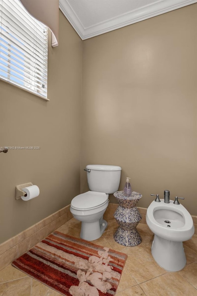 half bathroom featuring tile patterned floors, toilet, ornamental molding, a bidet, and baseboards