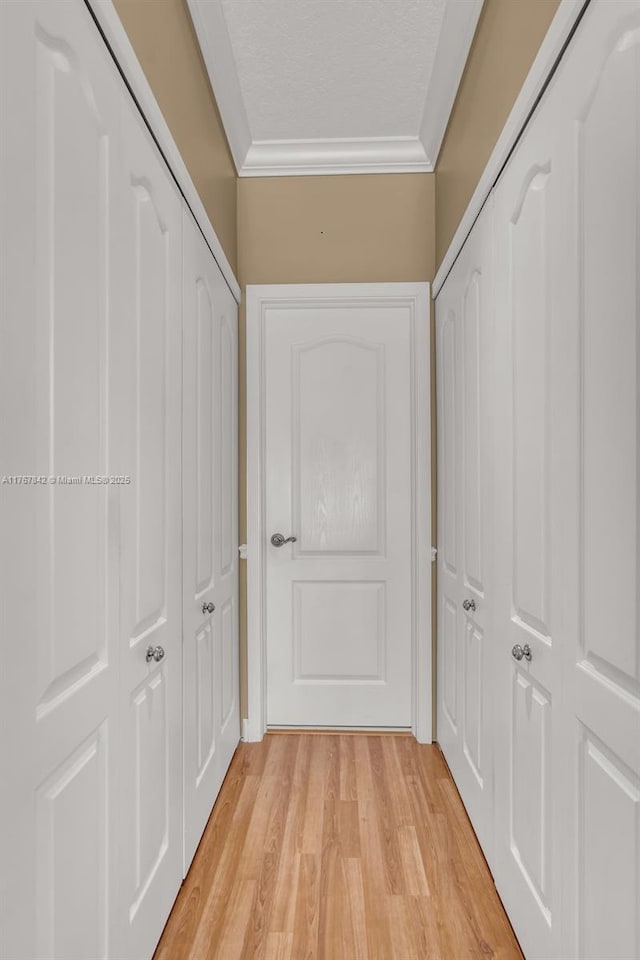 corridor with a textured ceiling, light wood-type flooring, and ornamental molding