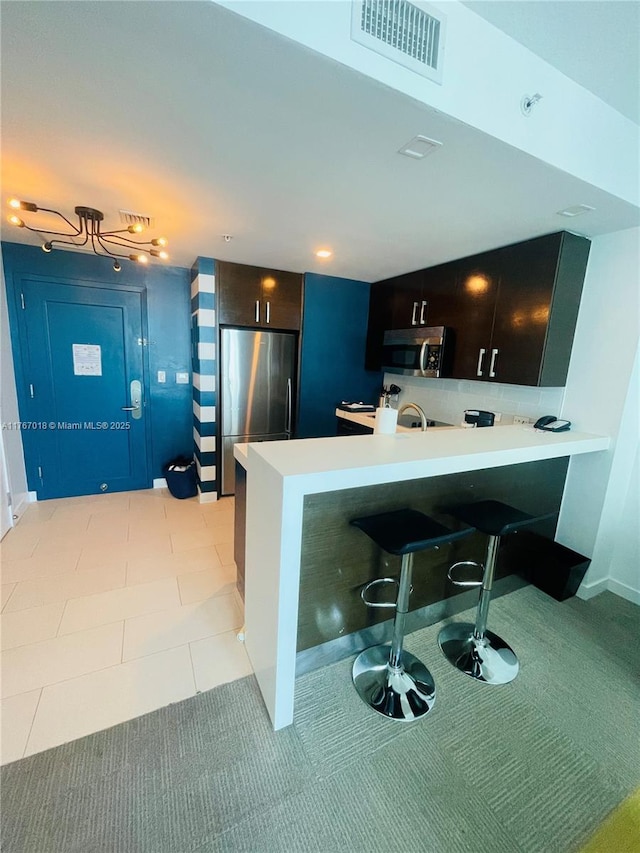kitchen featuring visible vents, a peninsula, a breakfast bar area, light countertops, and appliances with stainless steel finishes