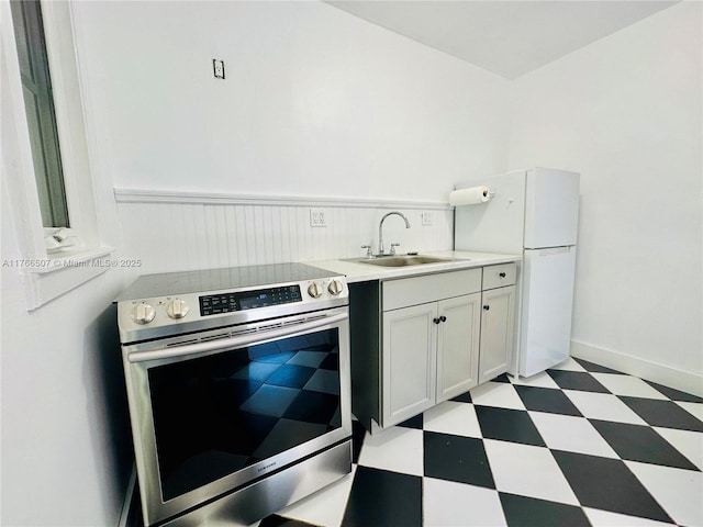 kitchen featuring light floors, freestanding refrigerator, a sink, light countertops, and electric stove