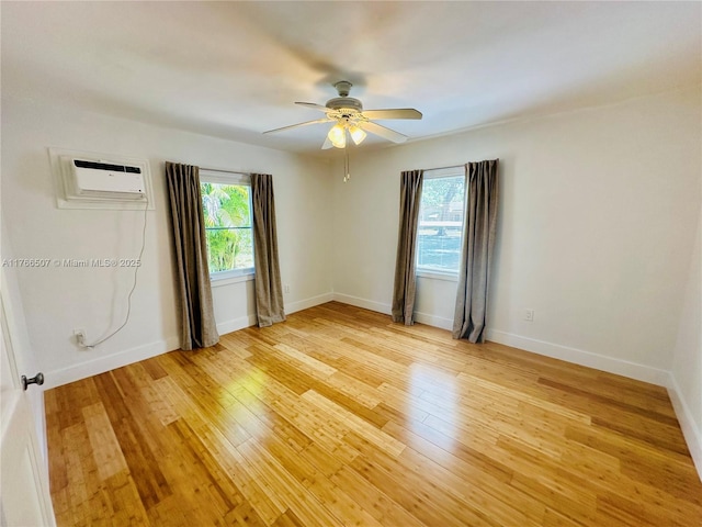 spare room with a wall unit AC, plenty of natural light, a ceiling fan, and light wood finished floors