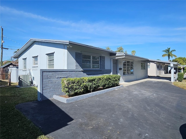 view of front of house with a front lawn, fence, stucco siding, central AC unit, and stone siding