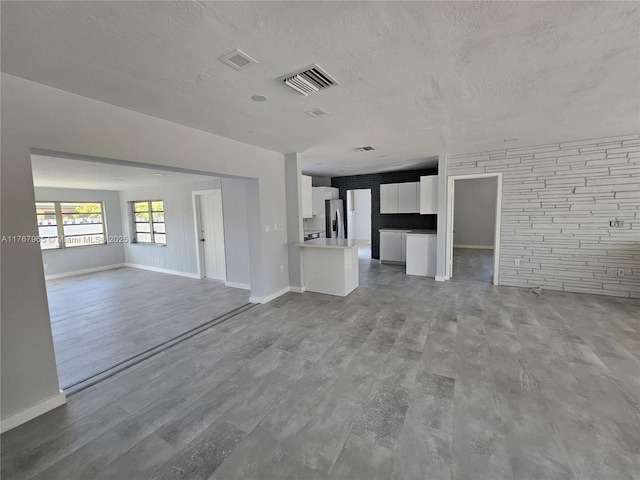 unfurnished living room featuring visible vents, baseboards, a textured ceiling, and wood finished floors
