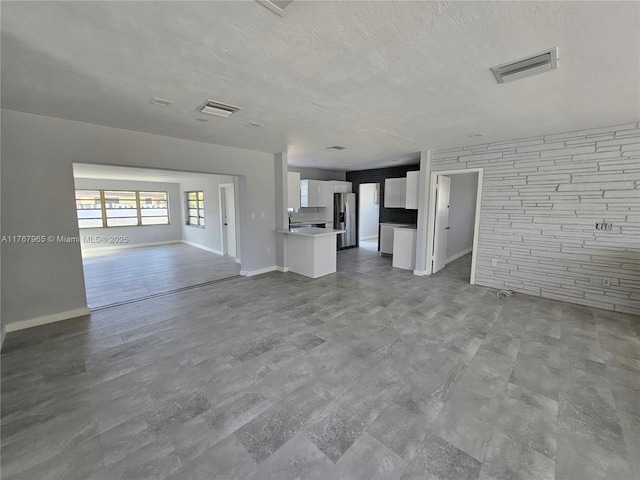 unfurnished living room with visible vents, a textured ceiling, and baseboards